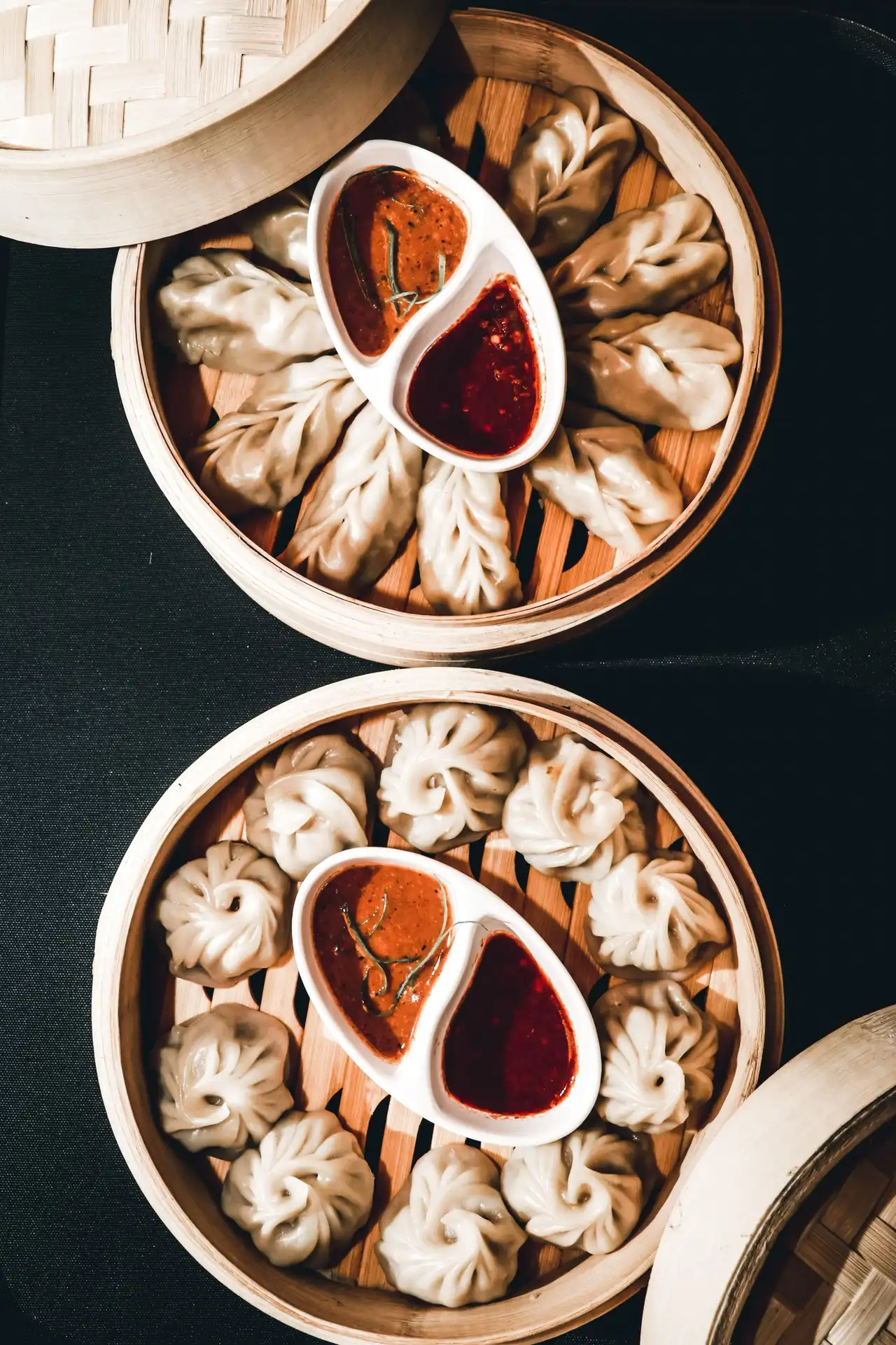Steamed momos in two bamboo steamers with dipping sauces