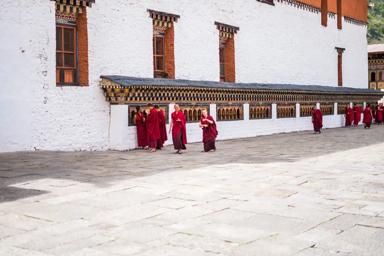 Monks in maroon robes walking beside the white wall of a dzong in Bhutan