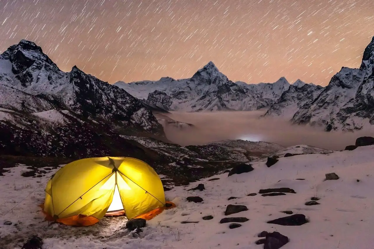 A glowing tent on snow beneath star trails, with Ama Dablam above