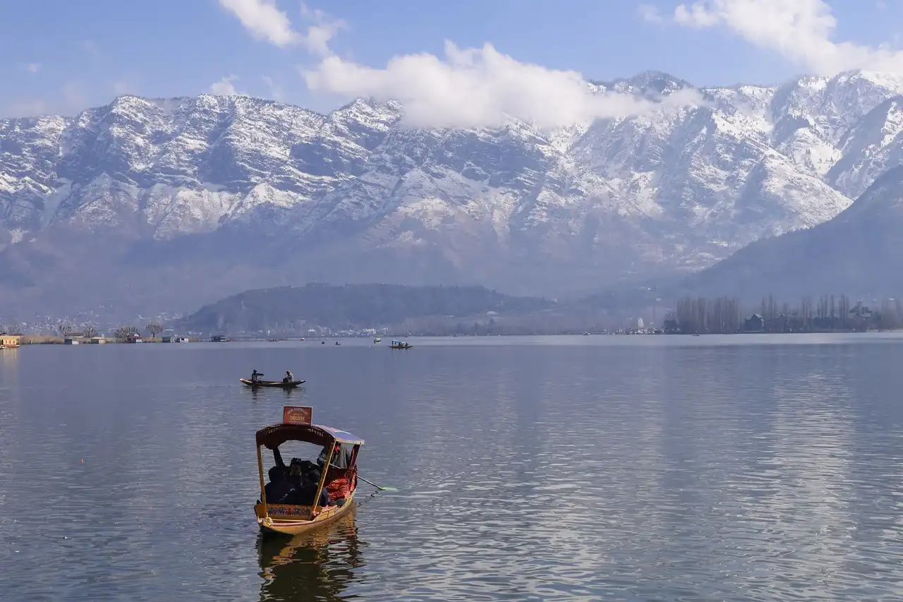 A red-canopied shikara crossing Dal Lake below snowy mountains