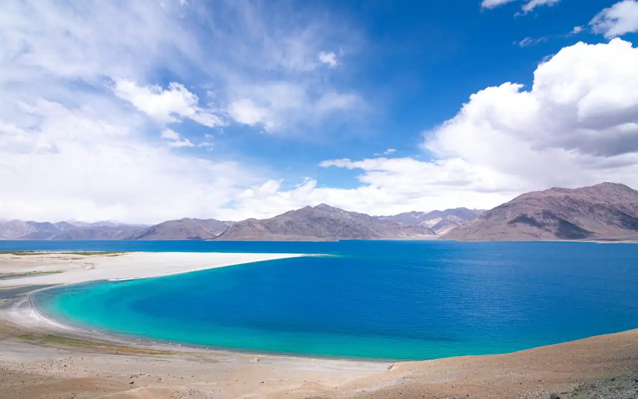 The turquoise lagoon of Pangong Tso curving along a pale shore below brown mountains