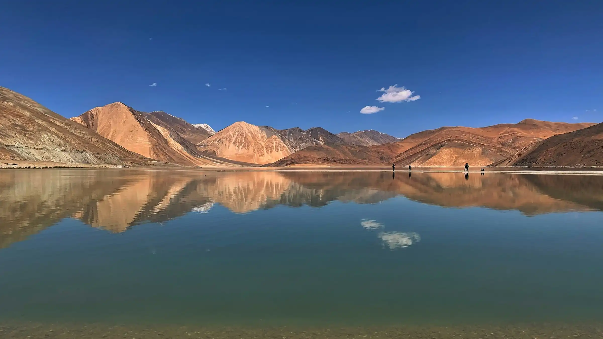 Ochre mountains reflected in the still blue water of Pangong Tso