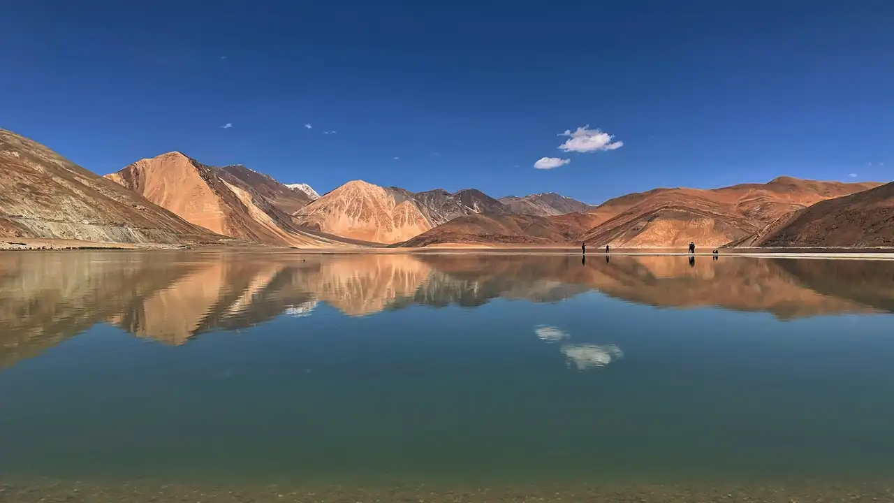 Ochre mountains reflected in the still blue water of Pangong Tso