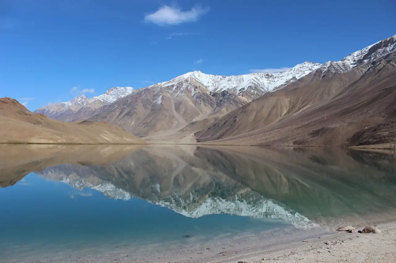 Bare slopes and snow peaks mirrored in Chandratal lake