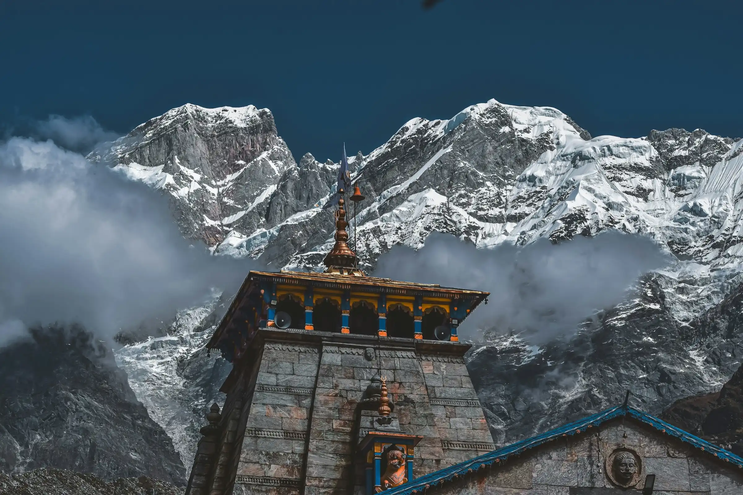 The stone spire of Kedarnath temple against cloud-wrapped snow peaks